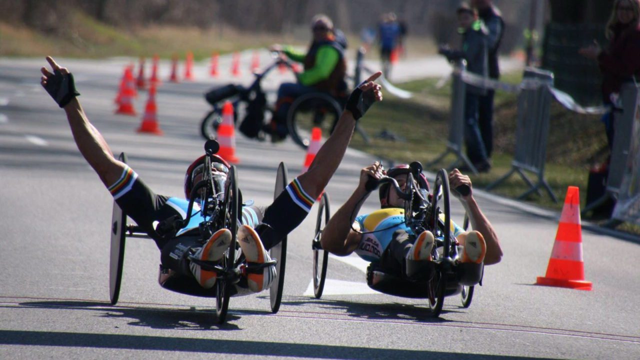 Two people riding a hand cycle with hands up