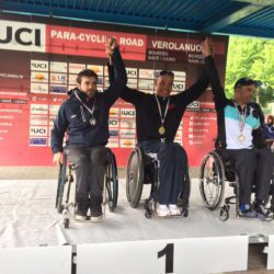 Three men in wheelchairs on a podium with medals.