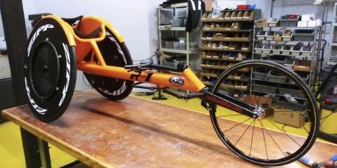 An orange wheelchair is sitting on a table in a workshop.