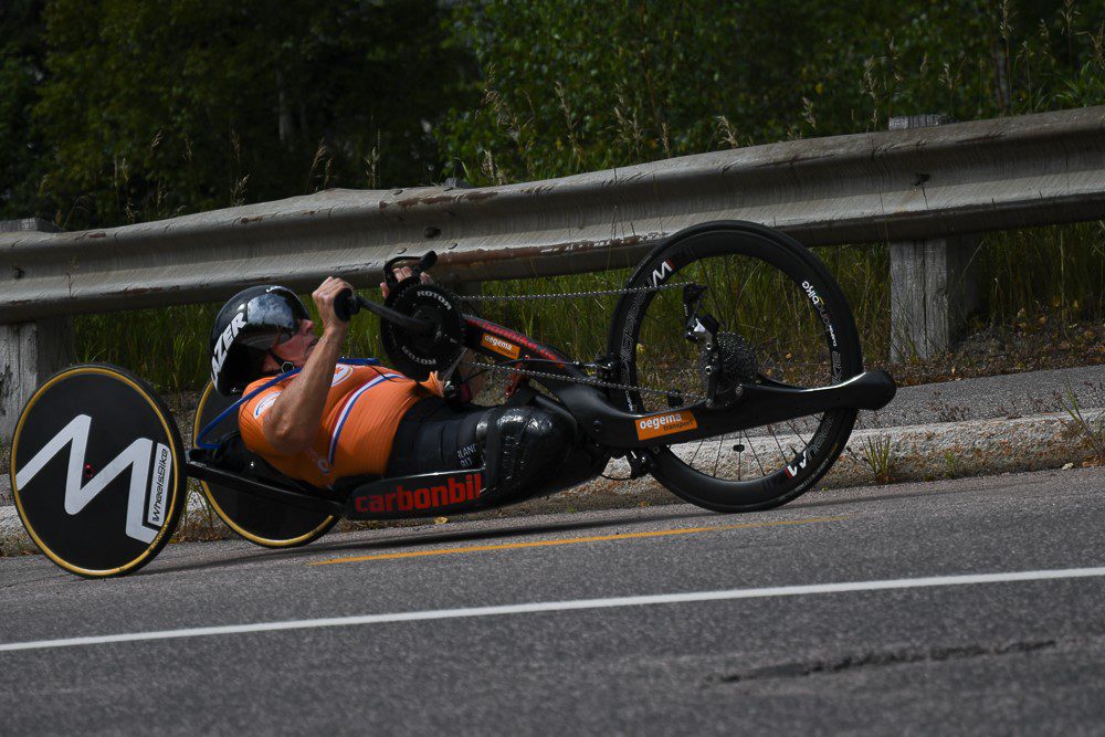 A man riding a hand cycle in orange Jersey at high speed