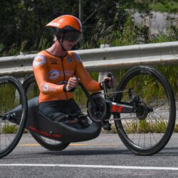 A lady wearing an orange jersey riding a carbon bike.