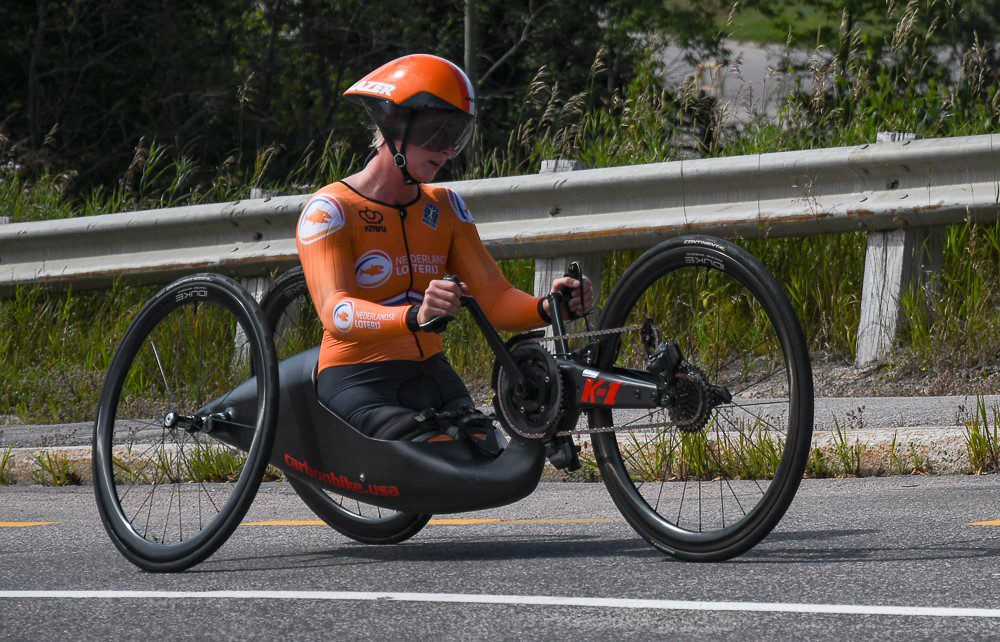 A lady wearing an orange jersey riding a carbon bike.