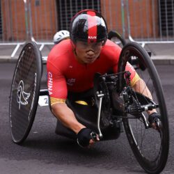 A man in a red and black outfit is riding a wheeled bicycle.
