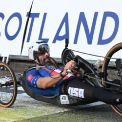 A man in a wheelchair laying on the ground in front of a scotland sign.